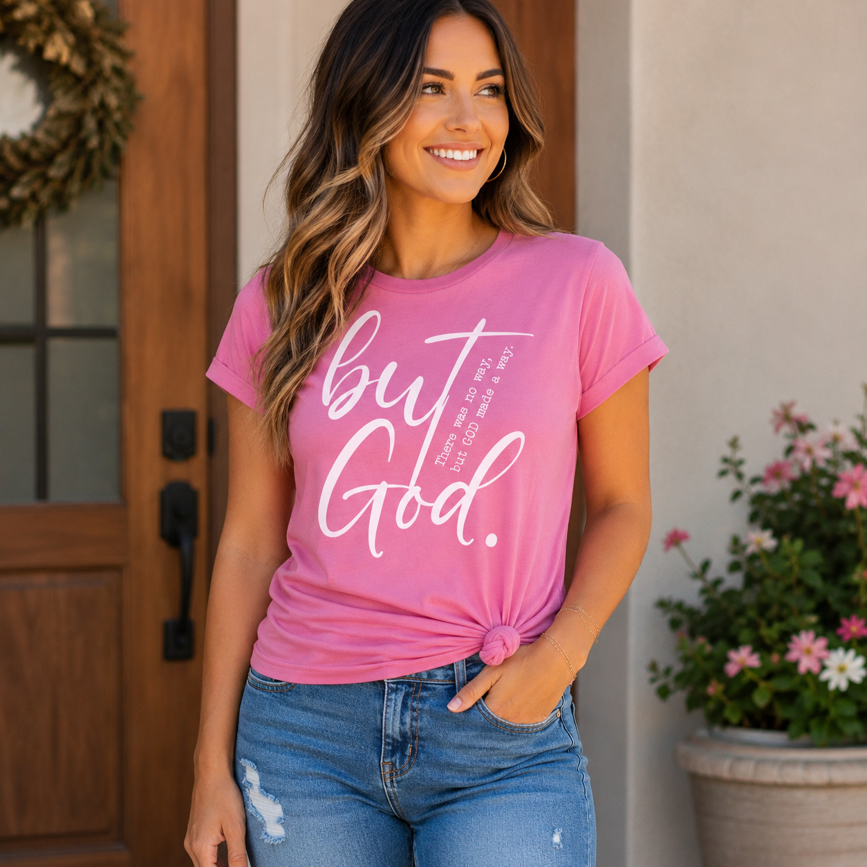 Woman wearing a pink t-shirt with 'but God' text, standing in front of a wooden door.
