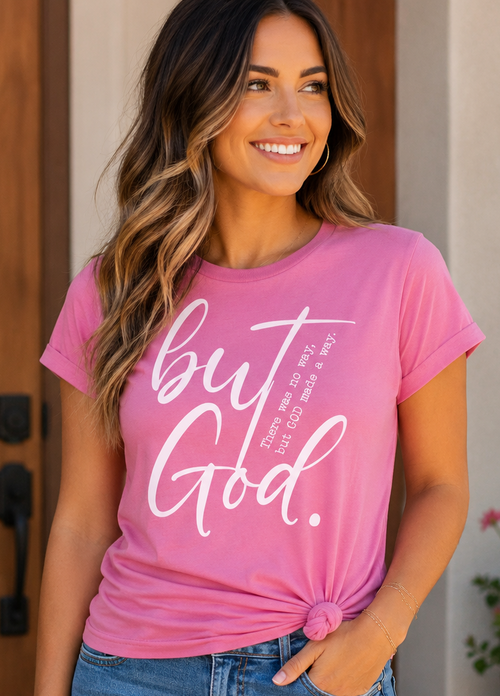 Woman wearing a pink t-shirt with 'but God' text, standing in front of a wooden door.